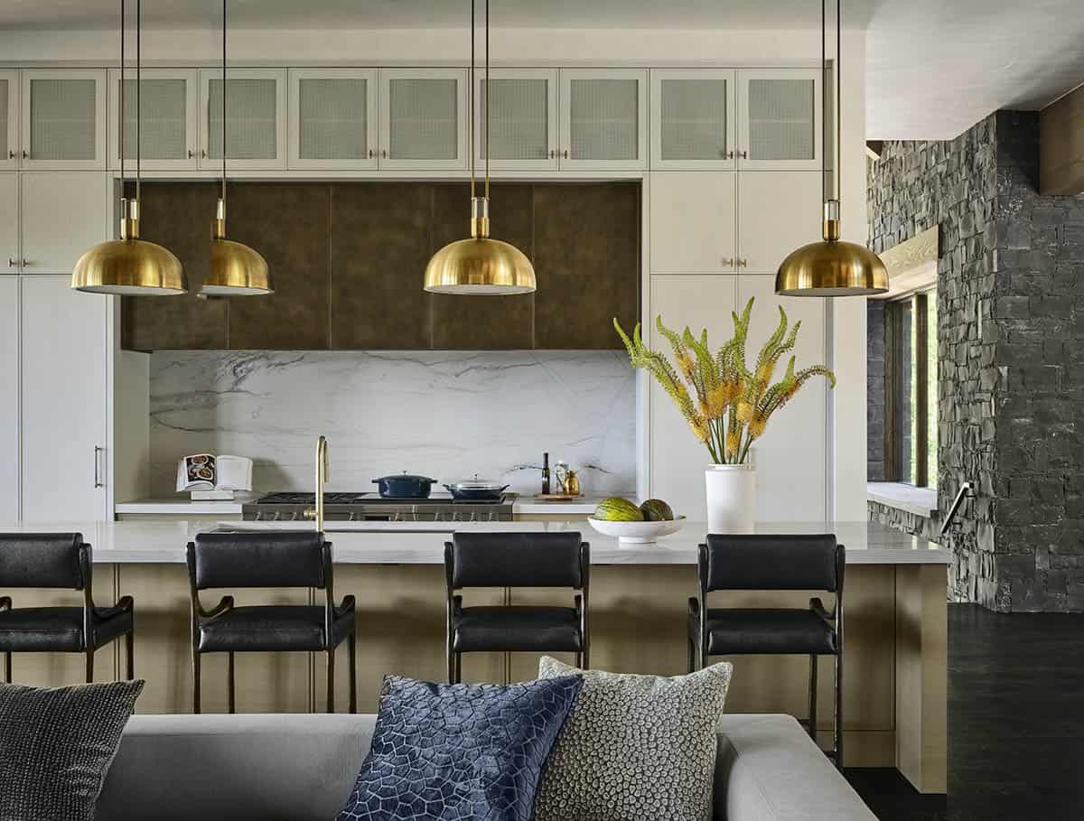 Kitchen with brass pendant lights, marble backsplash, and black leather chairs at island