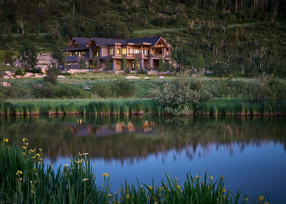 Mountain home exterior reflected in still pond surrounded by tall grasses
