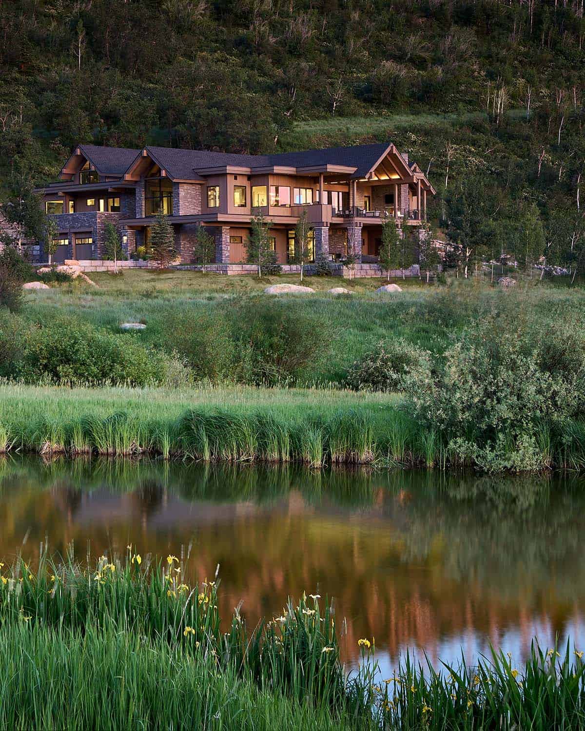 Stone-and-timber mountain house glowing at twilight above a reflective pond