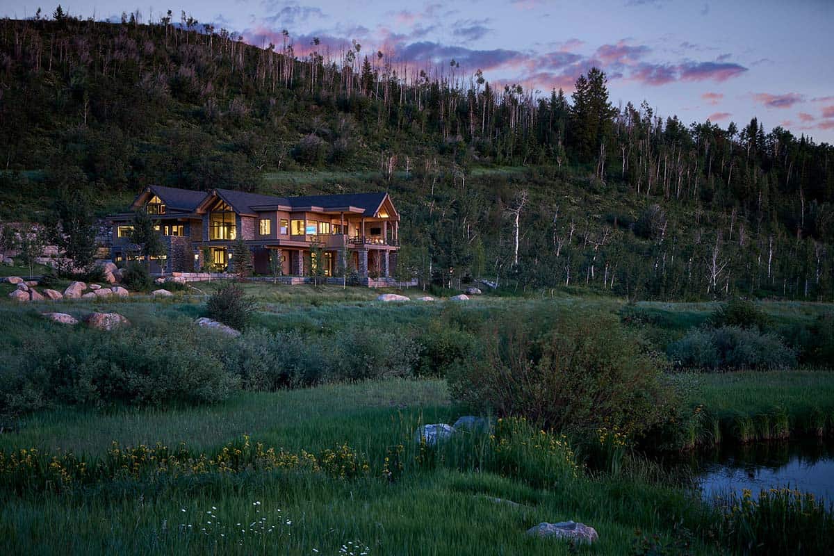 Wide landscape view of mountain retreat at dusk with pond and wildflowers