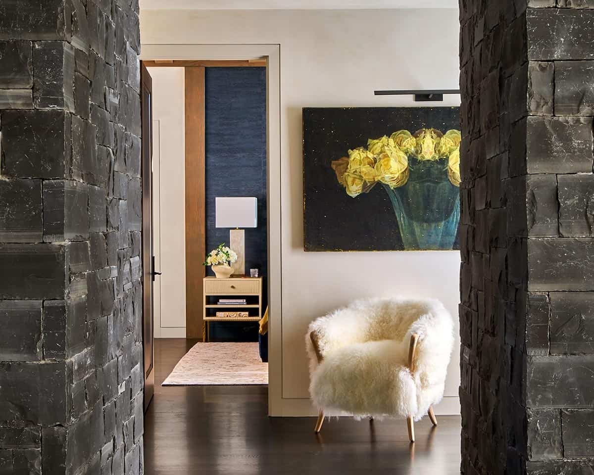 Hallway between dark stone columns leading to bedroom, with floral artwork and shearling chair