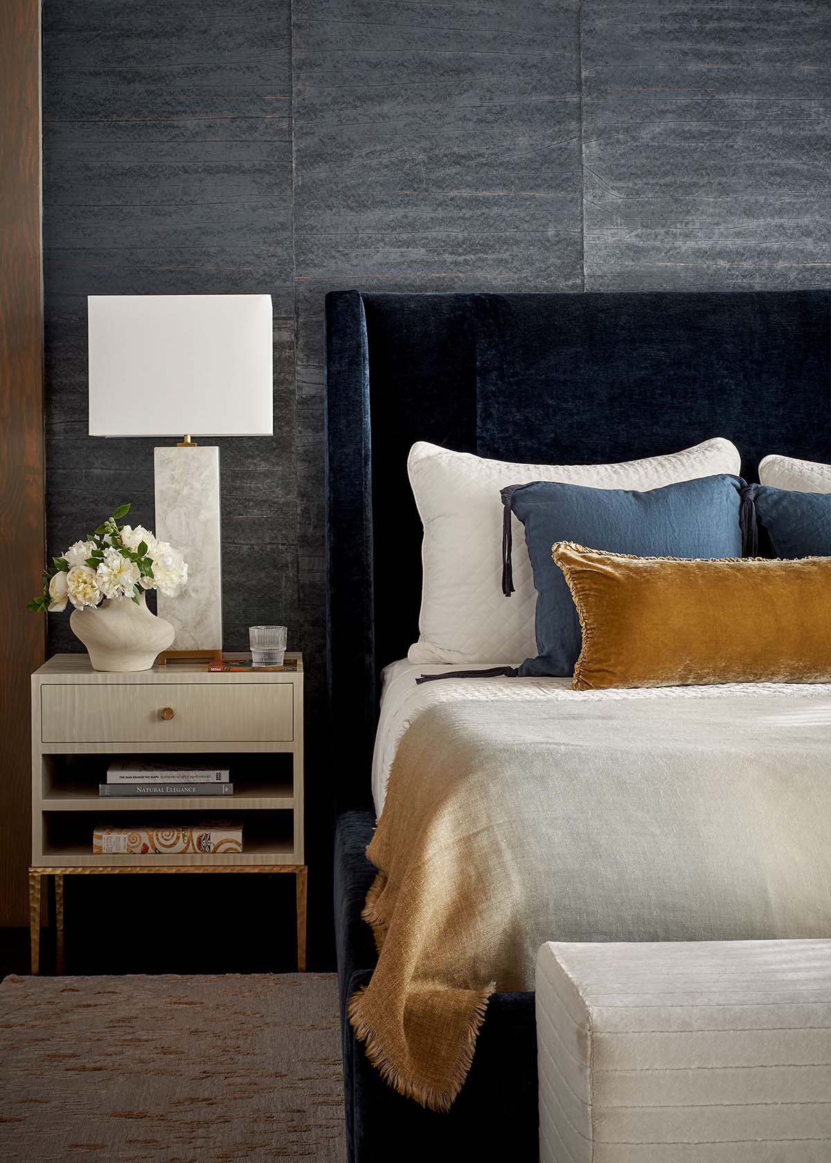 Bedroom detail with navy velvet headboard, mustard pillow, and marble table lamp