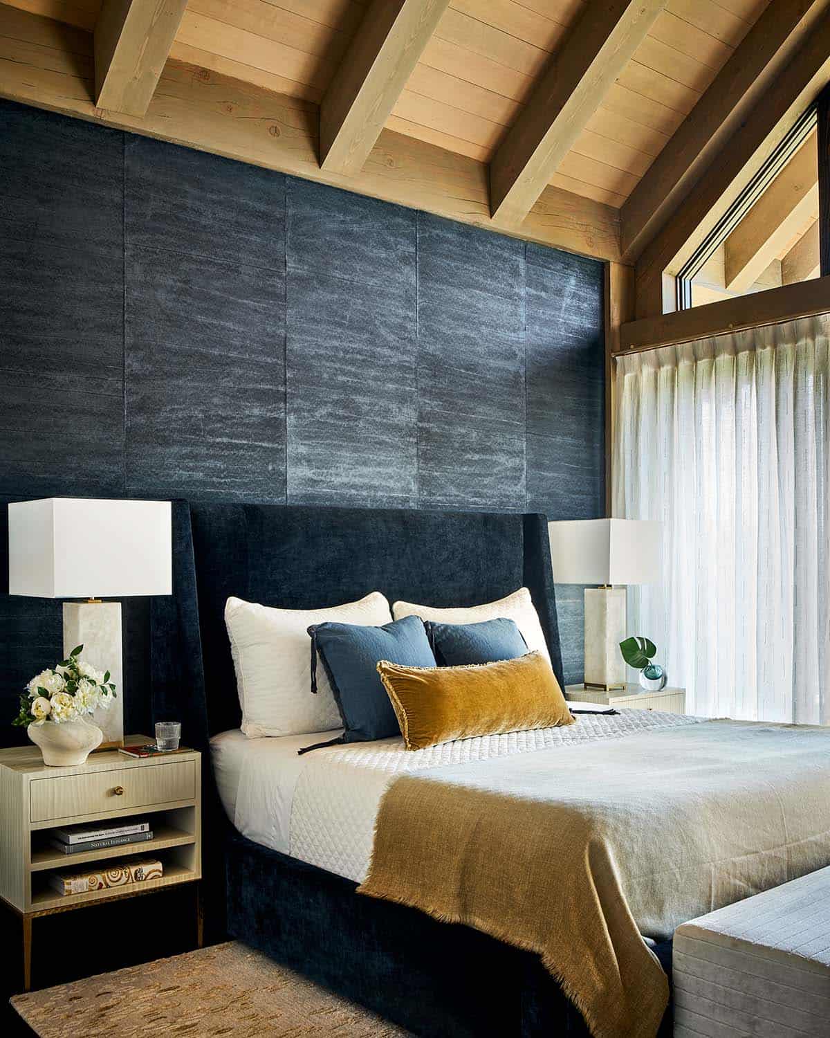 Bedroom with navy upholstered bed, wood-beam ceiling, and sheer curtains