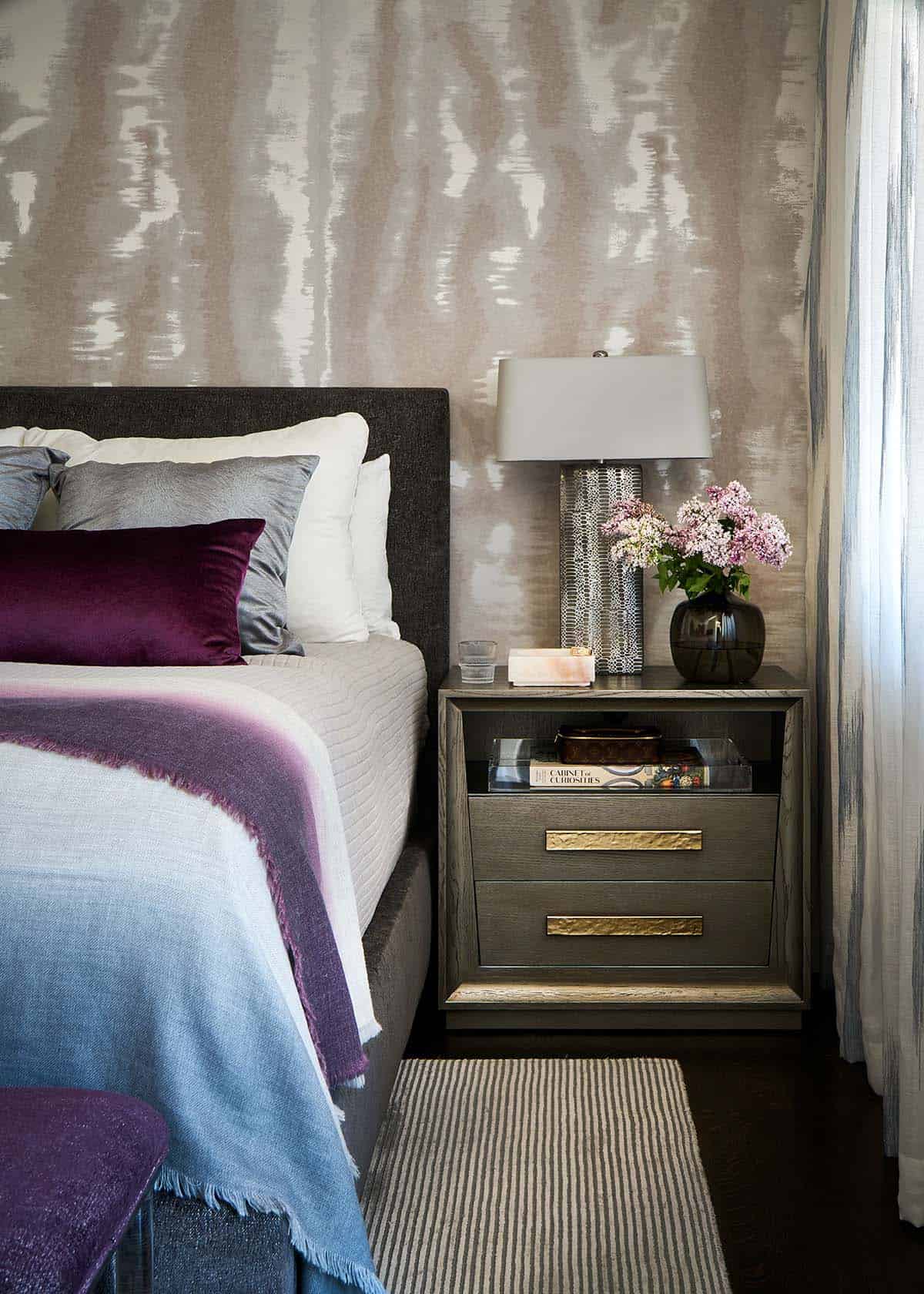 Bedroom nightstand with striped rug, table lamp, and purple velvet pillow