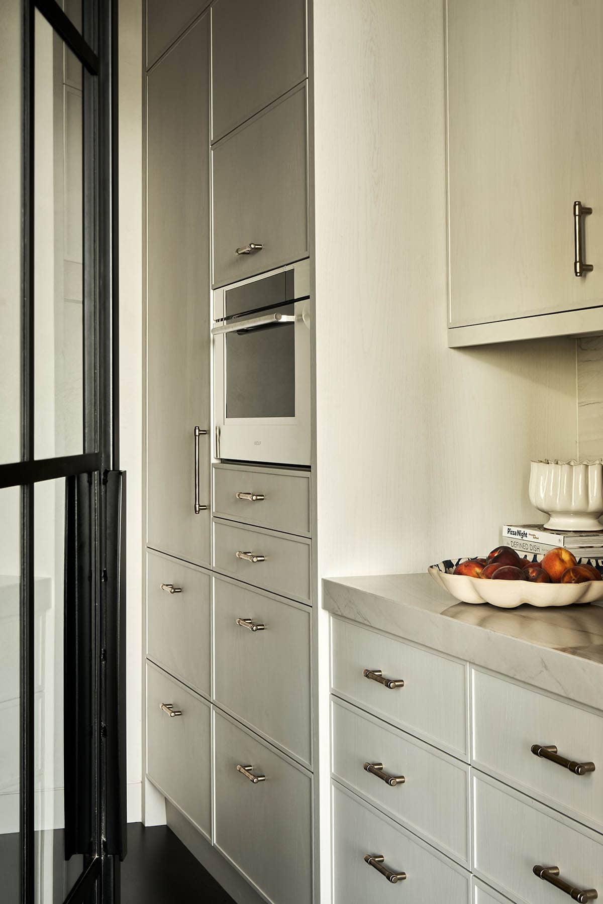 Kitchen cabinetry detail with built-in oven, brass hardware, and marble counter