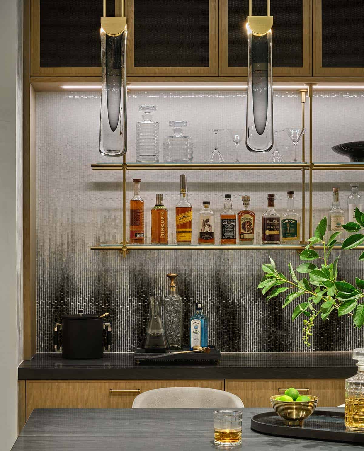Close-up of wet bar shelving with decanters, liquor bottles, and mosaic tile backsplash