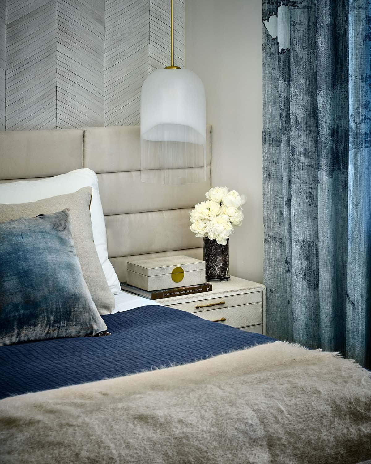 Bedroom nightstand detail with white pendant light, chevron wood accent wall, and blue curtain