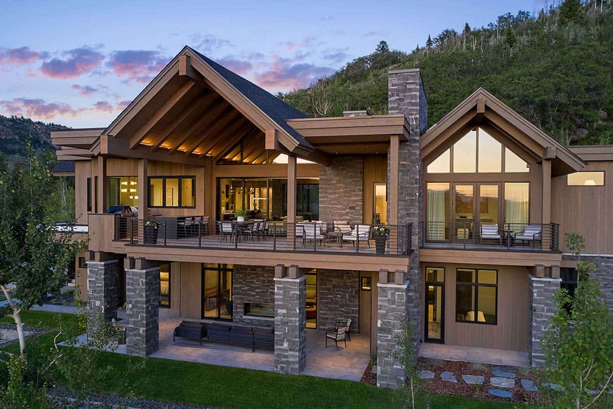 Aerial view of mountain home exterior with wraparound deck at sunset