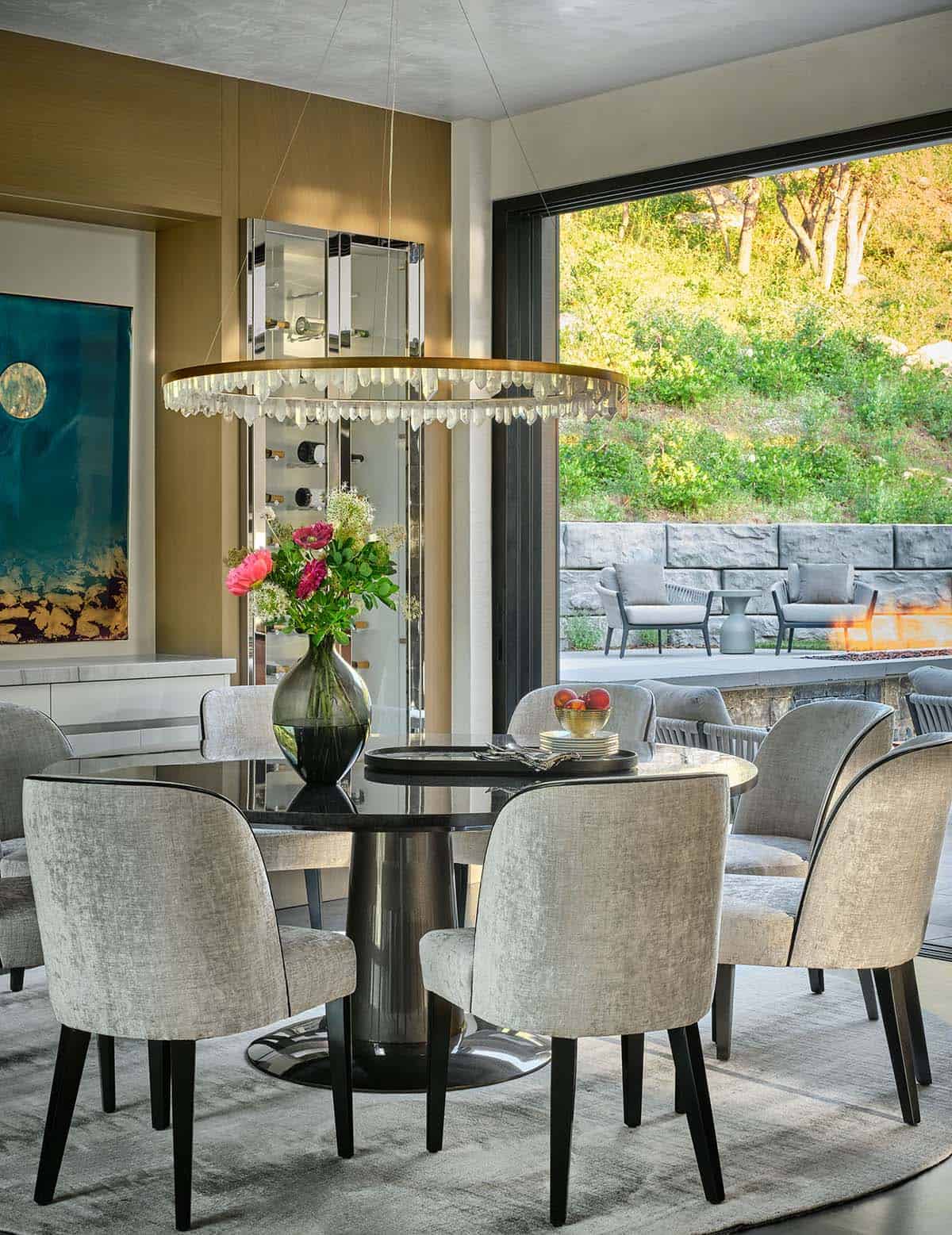 Round dining table with gray chairs beneath a crystal chandelier, opening to outdoor patio