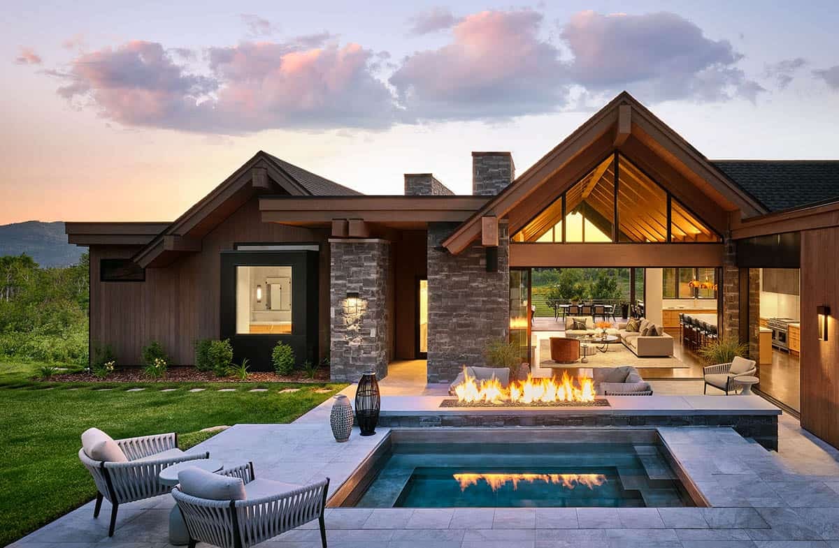 Rear exterior of mountain home with pool, fire feature, and open living space at sunset