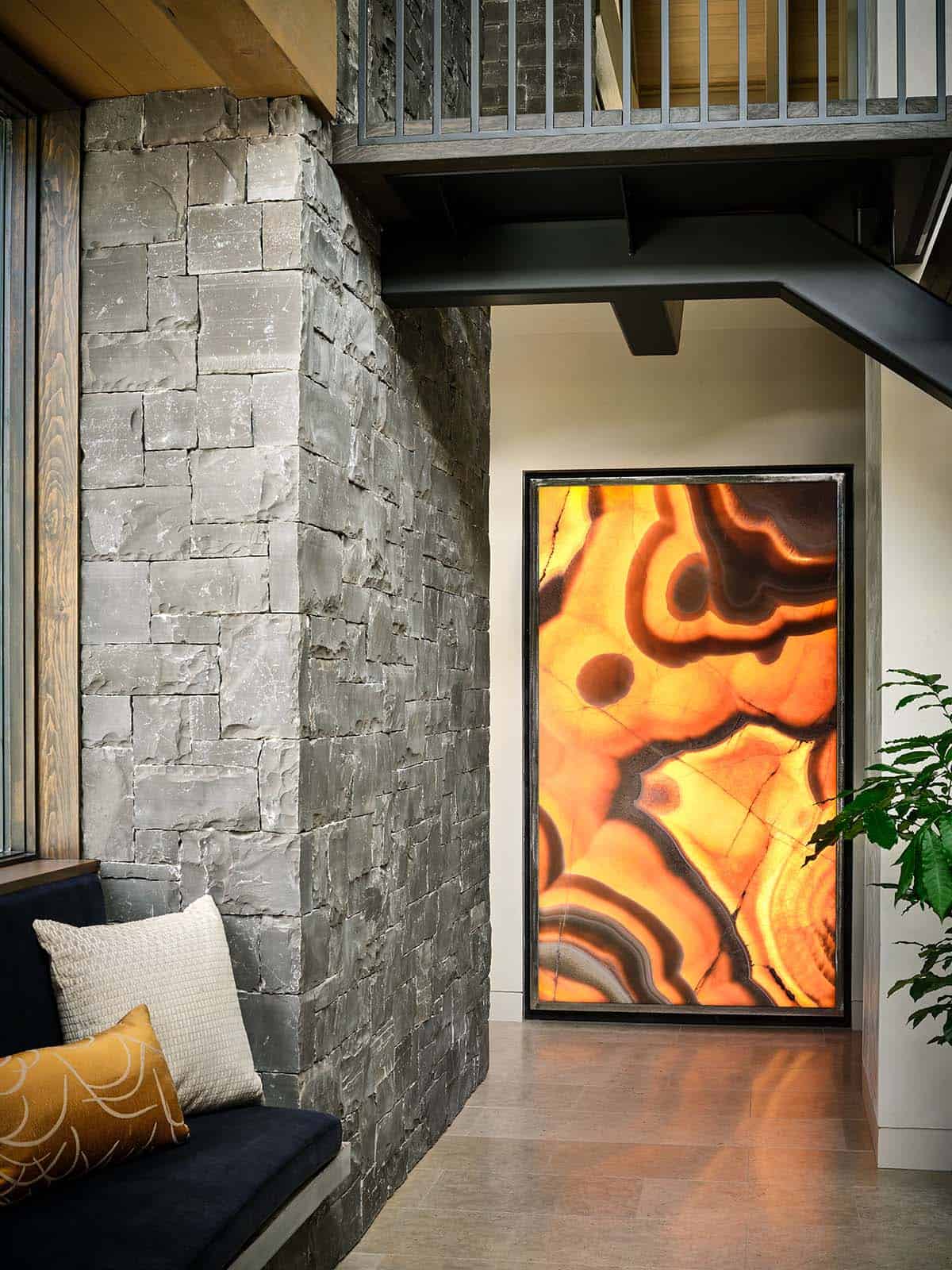 Backlit onyx art panel glowing orange beside stacked-stone wall and staircase