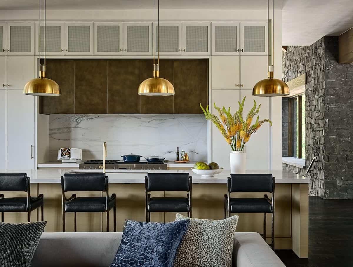 Kitchen island with brass pendant lights, black chairs, and marble backsplash