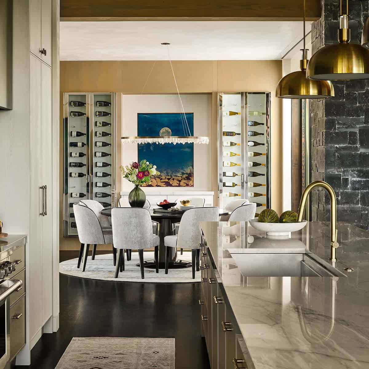 Dining area with round table, gray chairs, and glass wine cabinets flanking artwork