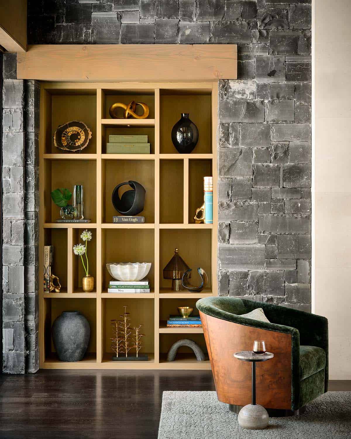 Built-in bookshelf styled with vases, sculptures, and books beside a green velvet chair