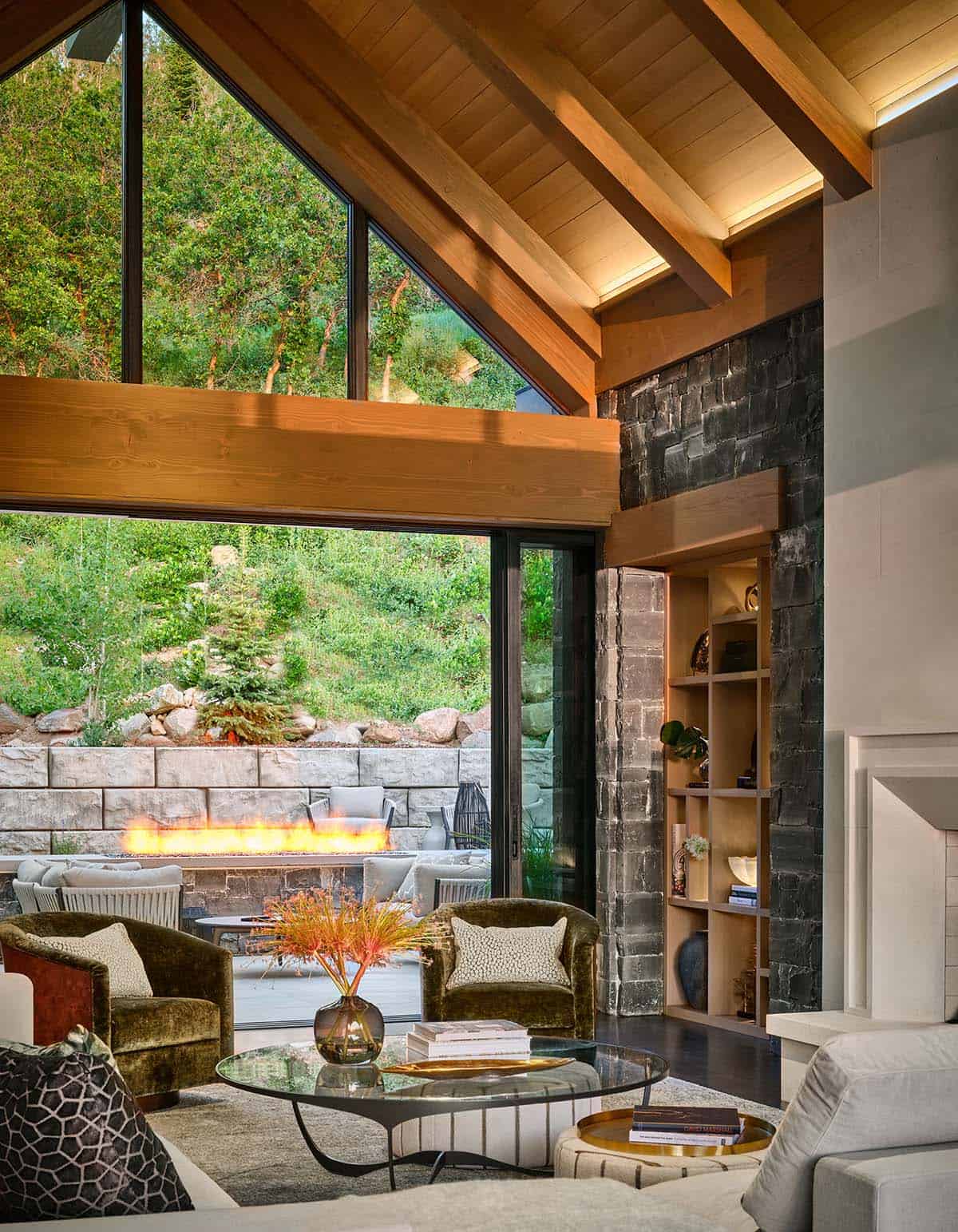 Living room corner with green velvet chairs, glass doors open to outdoor fire pit
