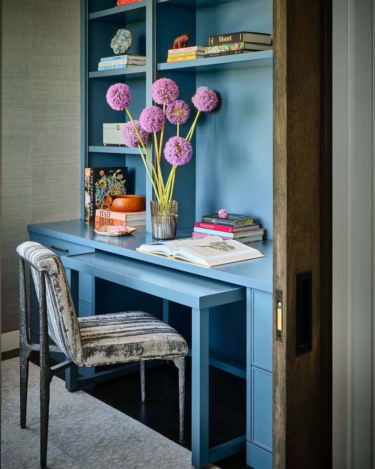 Blue built-in desk nook with striped chair and vase of purple allium flowers