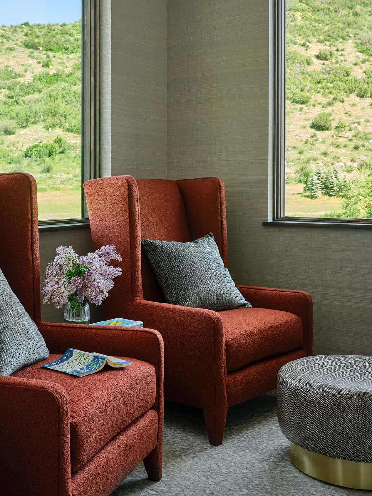 Rust-colored wingback chairs by a window with a small vase of lilacs