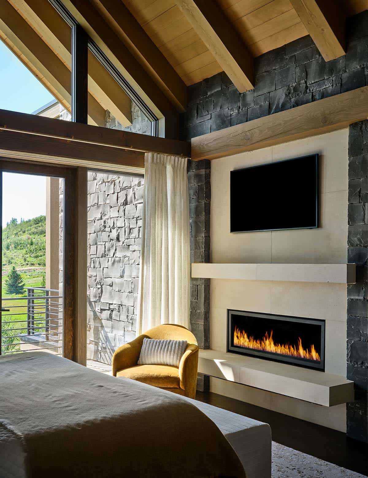 Bedroom with linear fireplace, TV, and yellow accent chair by a window