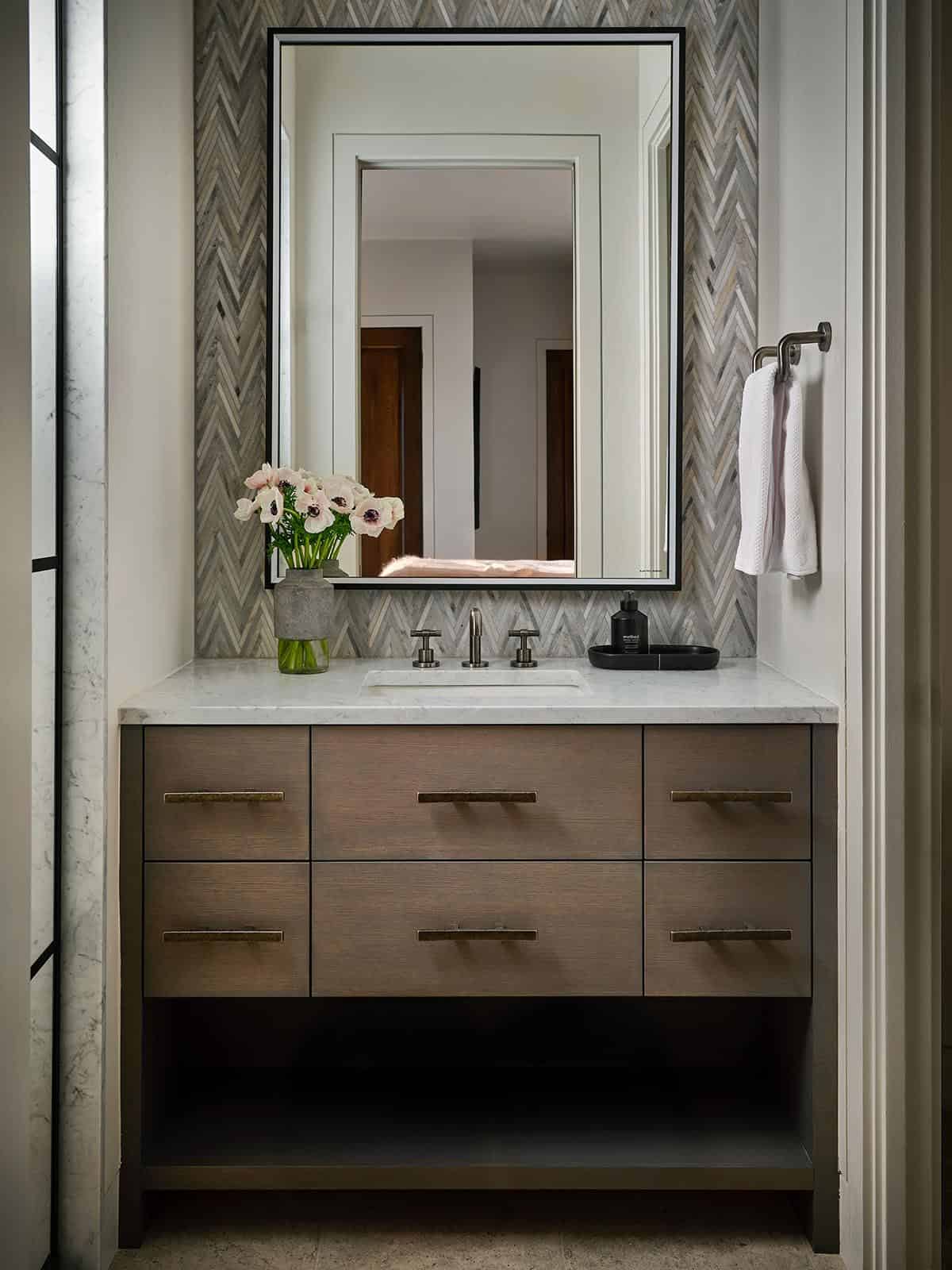 Powder room vanity with herringbone tile wall and round mirror