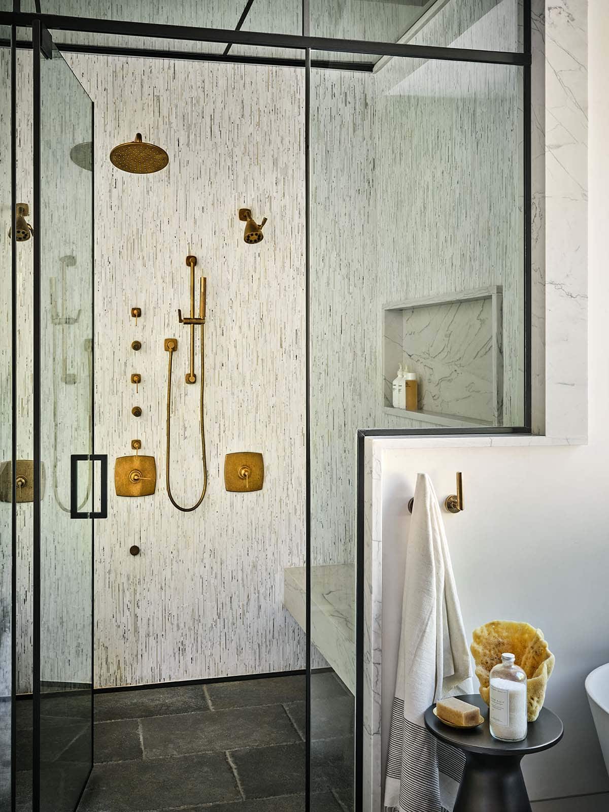 Walk-in shower with brass fixtures, textured tile walls, and marble niche
