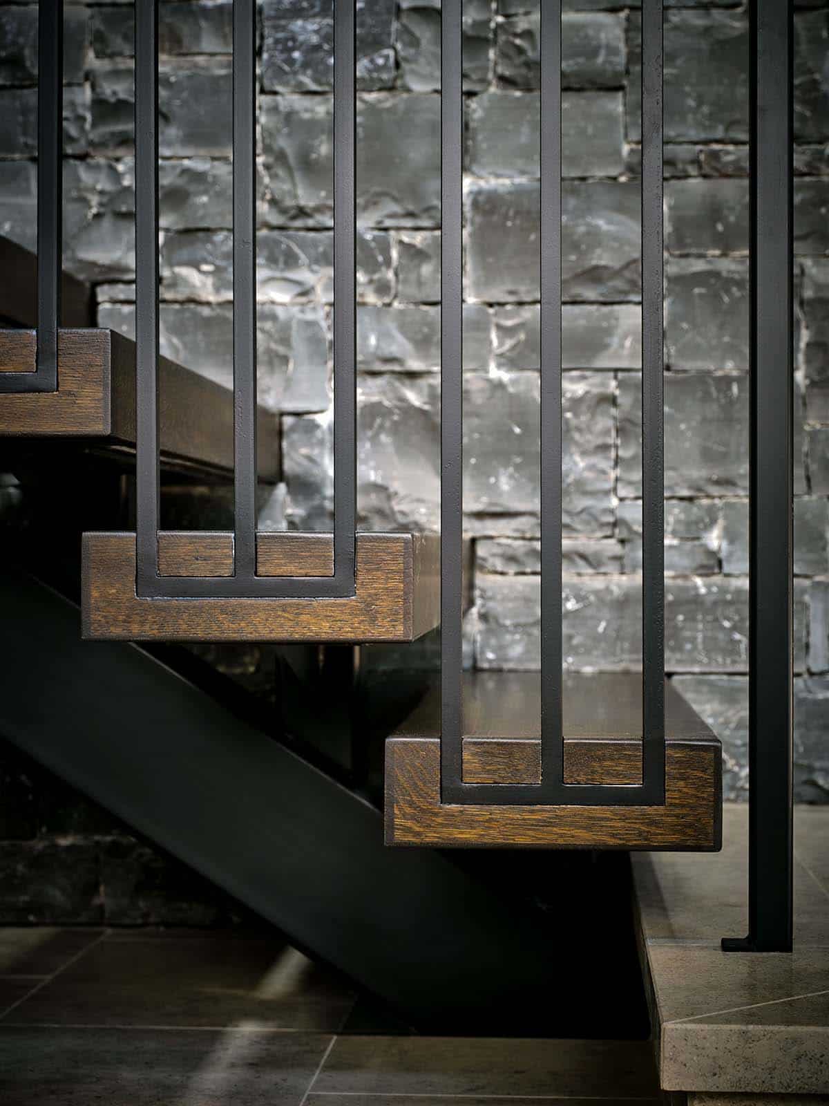 Close-up of dark wood stair treads with black metal railing against stone wall