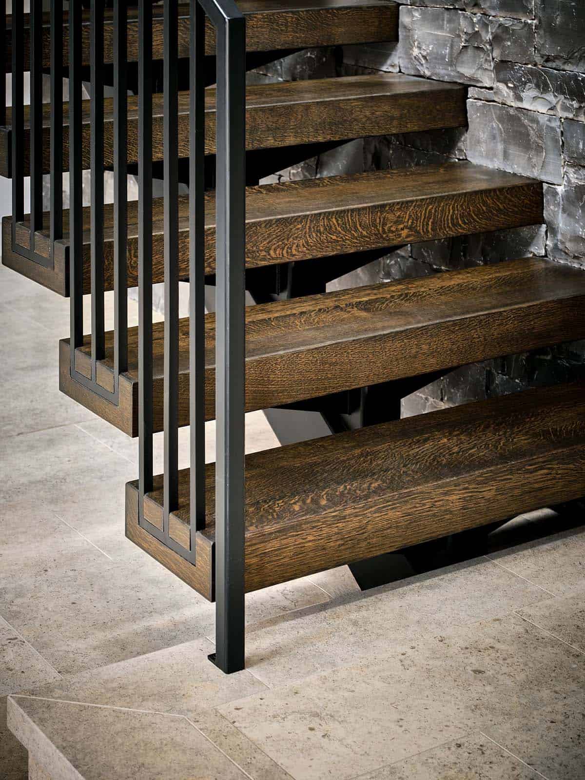 Close-up of floating wood stair treads with black metal railing against a stacked-stone wall
