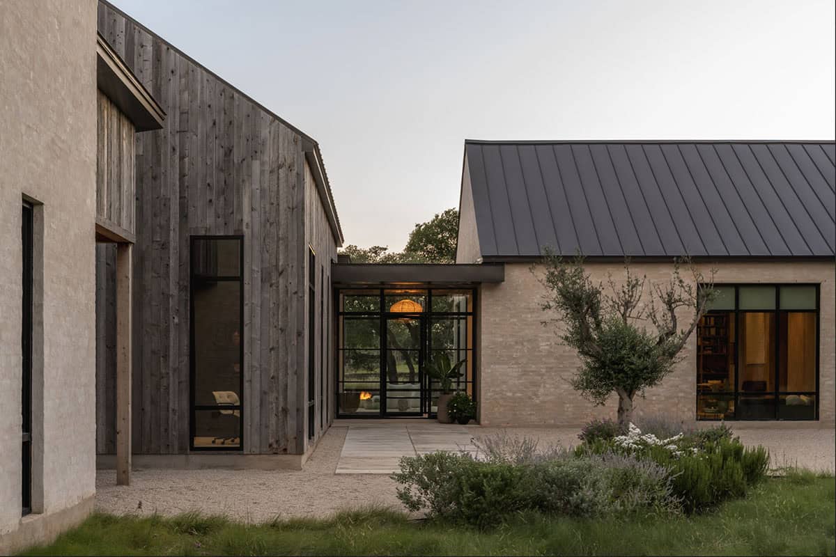 Covered walkway links the dark wood volume to the warm-lit study