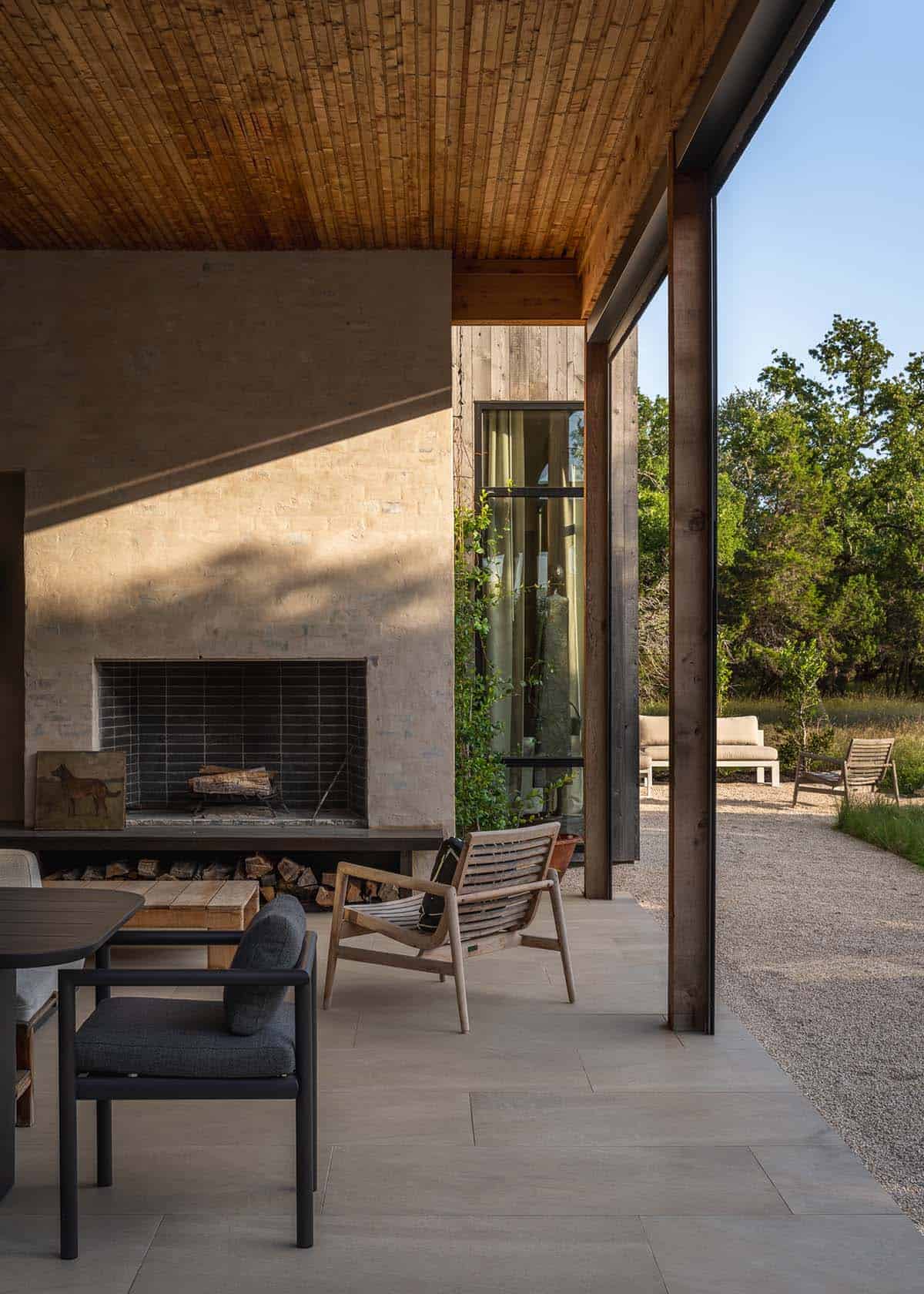 Covered patio with outdoor fireplace and teak furniture overlooks the gravel yard