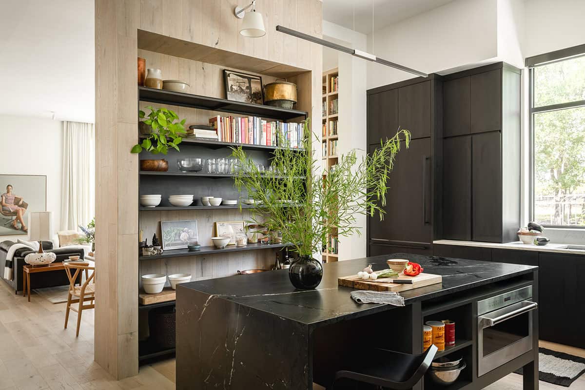 Black marble kitchen island stands before open shelving and dark cabinetry