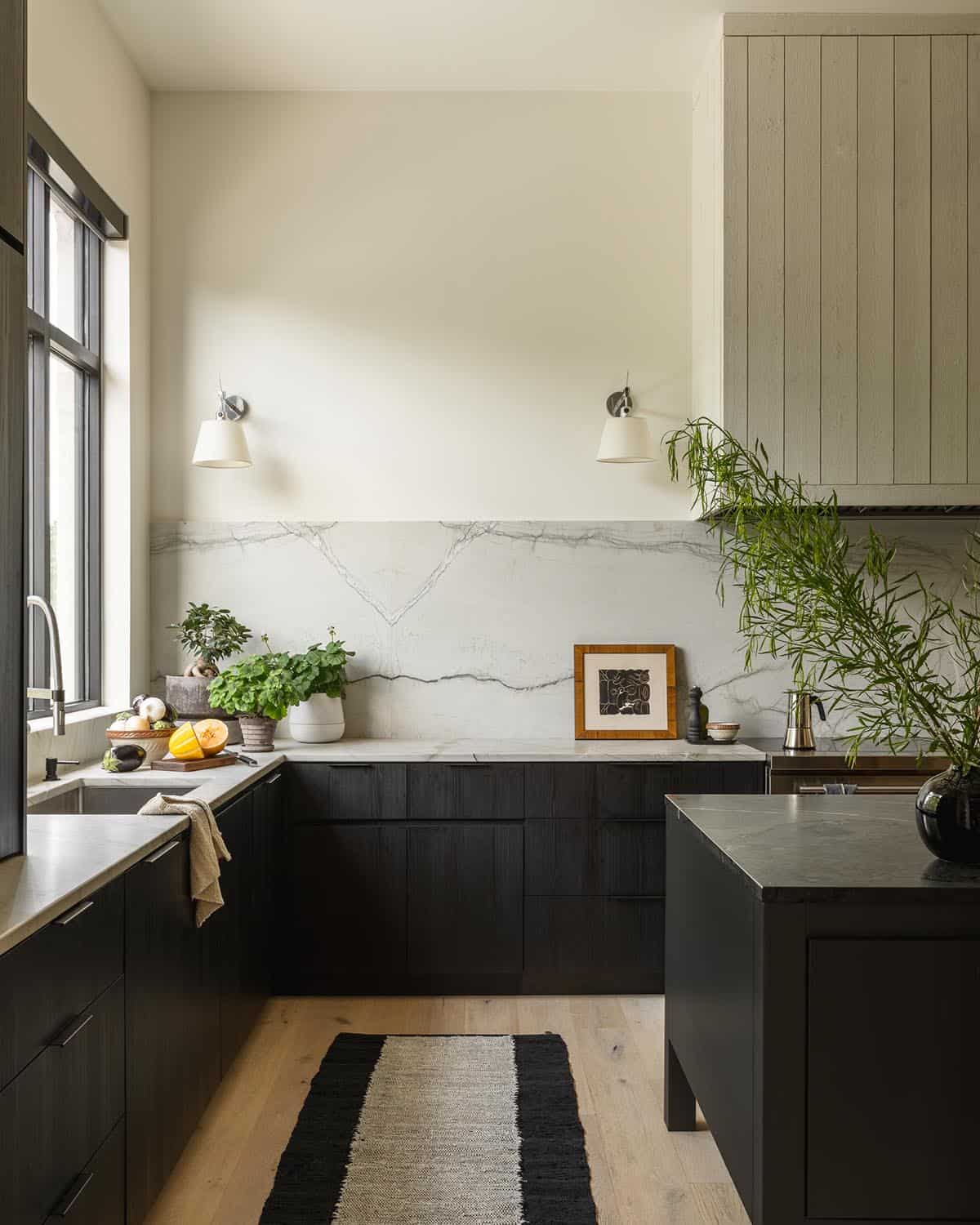 Dark kitchen cabinetry with veined marble backsplash and layered wall sconces
