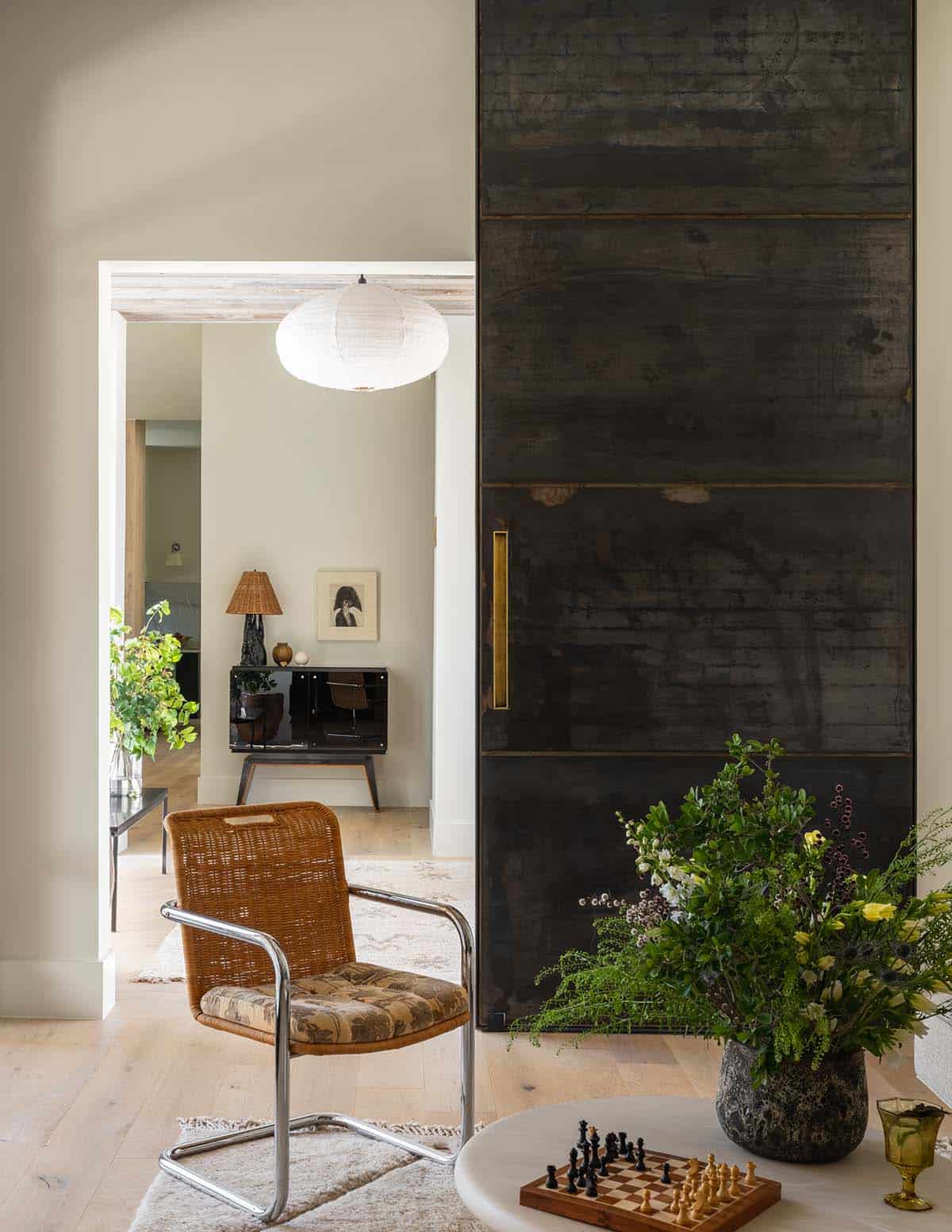 Blackened steel sliding door opens toward a wicker chair and pendant light