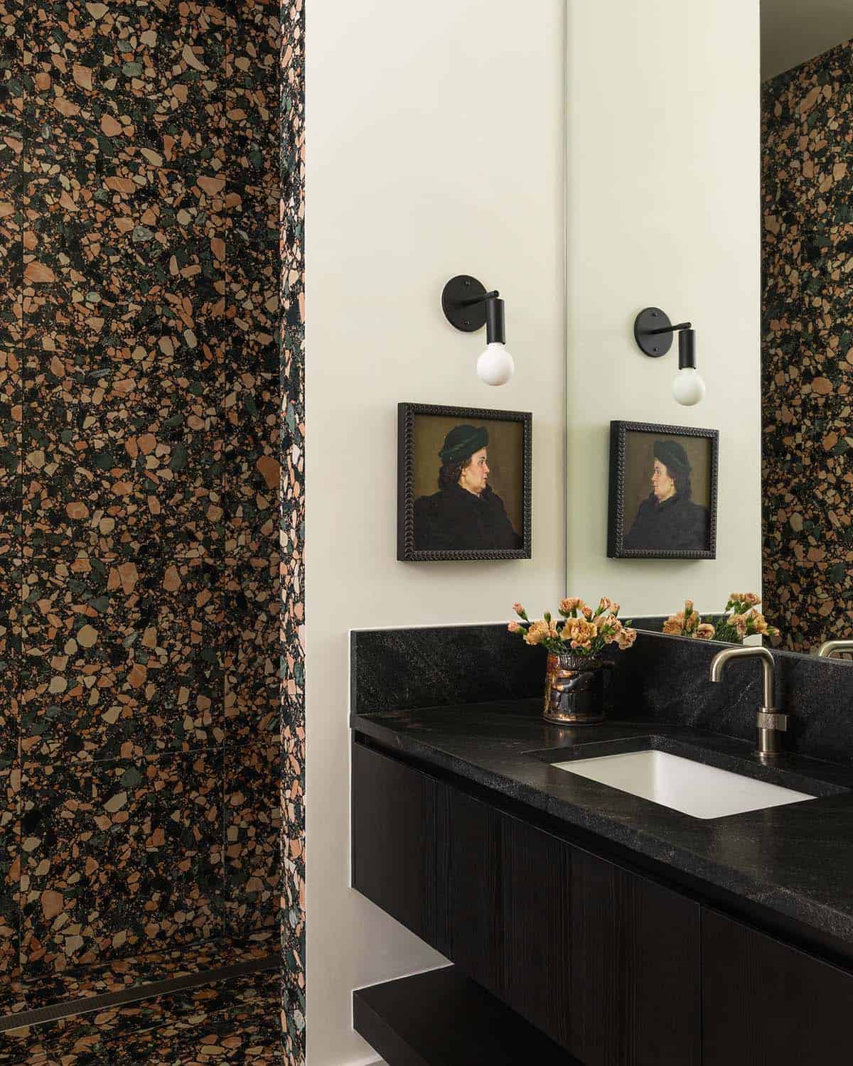 Terrazzo shower wall beside a black stone vanity with framed portrait