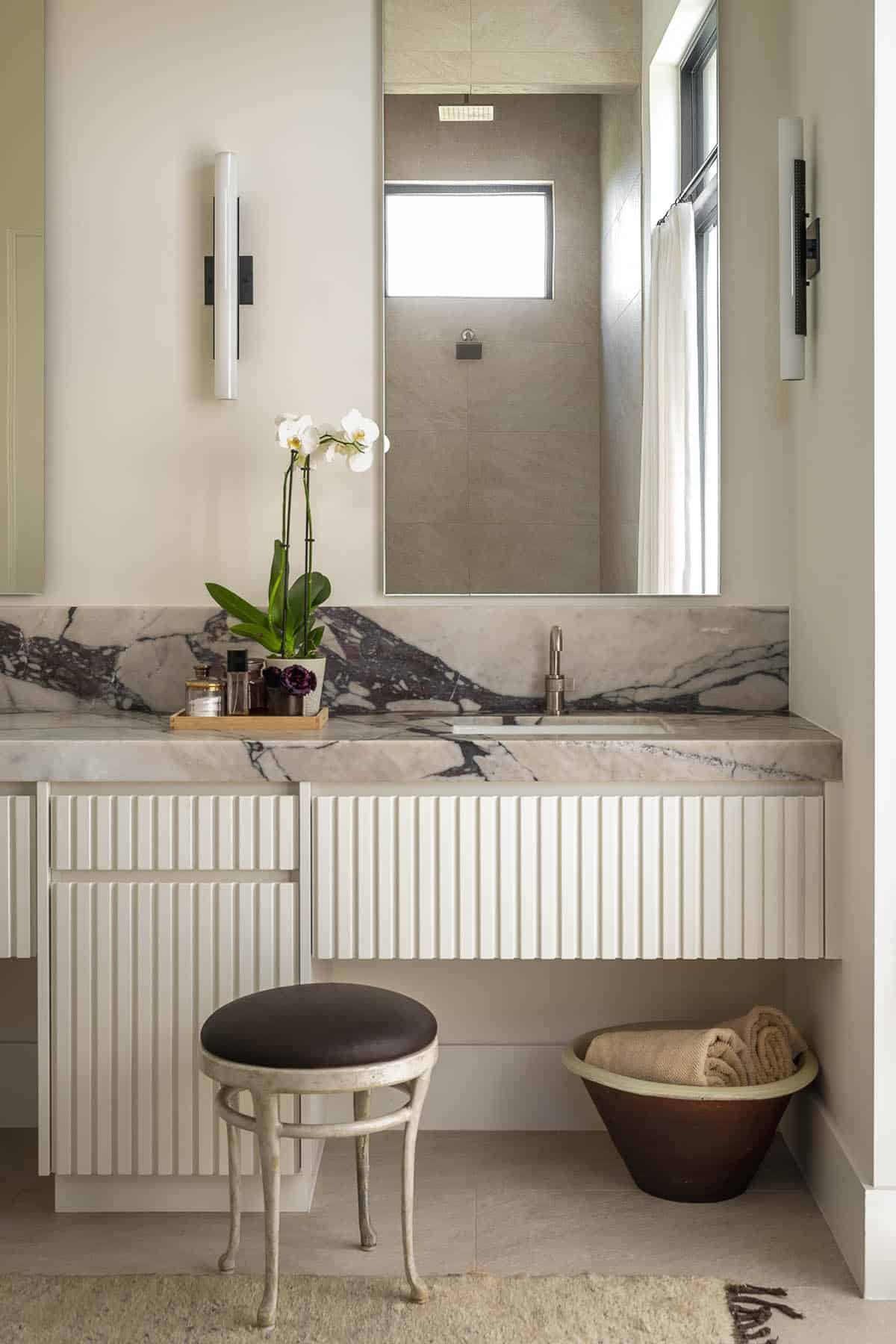 Primary bathroom with fluted white cabinetry and veined marble countertop