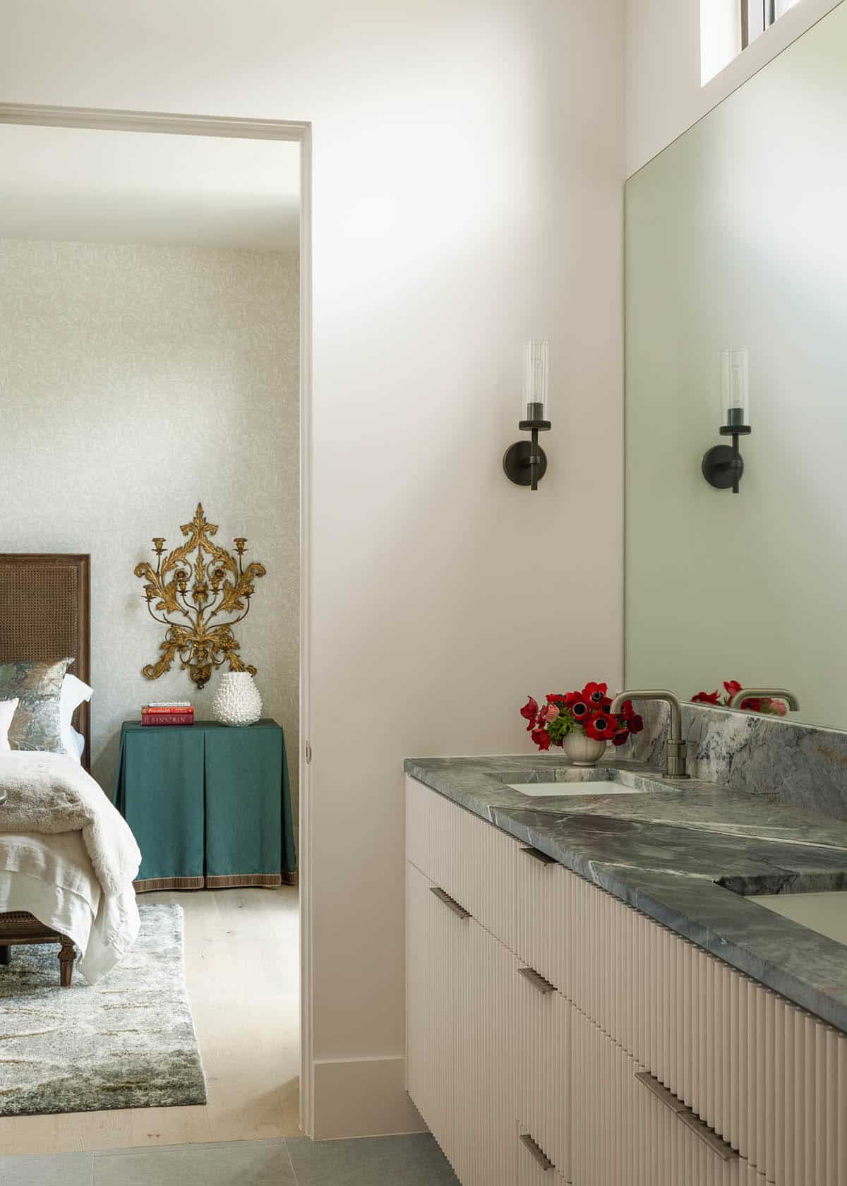 Green marble vanity glimpsed from a bedroom with a skirted nightstand