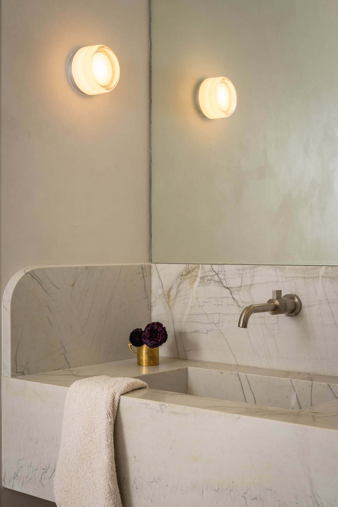 Marble trough sink beneath twin sconces and a frameless mirror