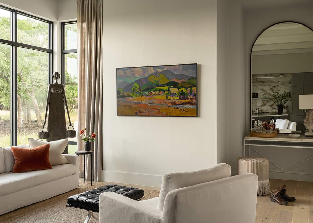 Living room armchairs face a landscape painting beside an arched mirror