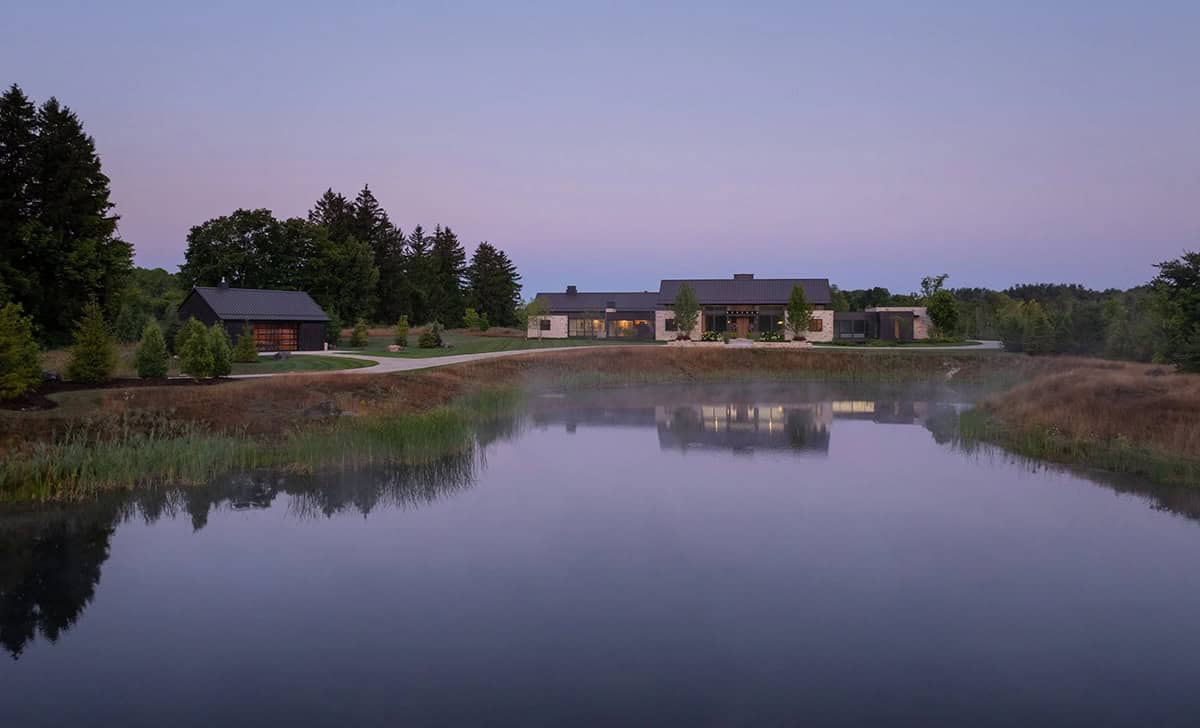 Modern countryside home at dusk reflected in a still pond, surrounded by trees
