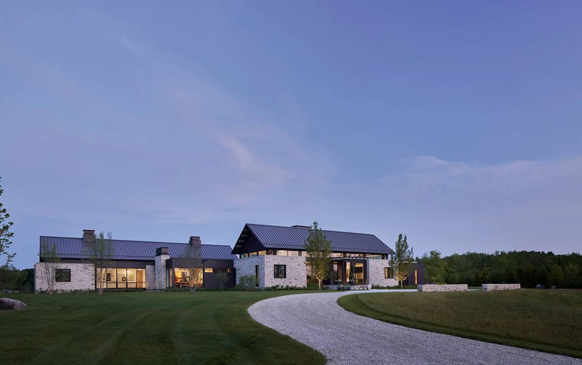 Modern countryside home with stone and metal-roofed pavilions at dusk
