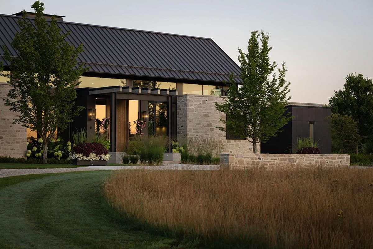 Stone and black-paneled home exterior with entry pergola at sunset