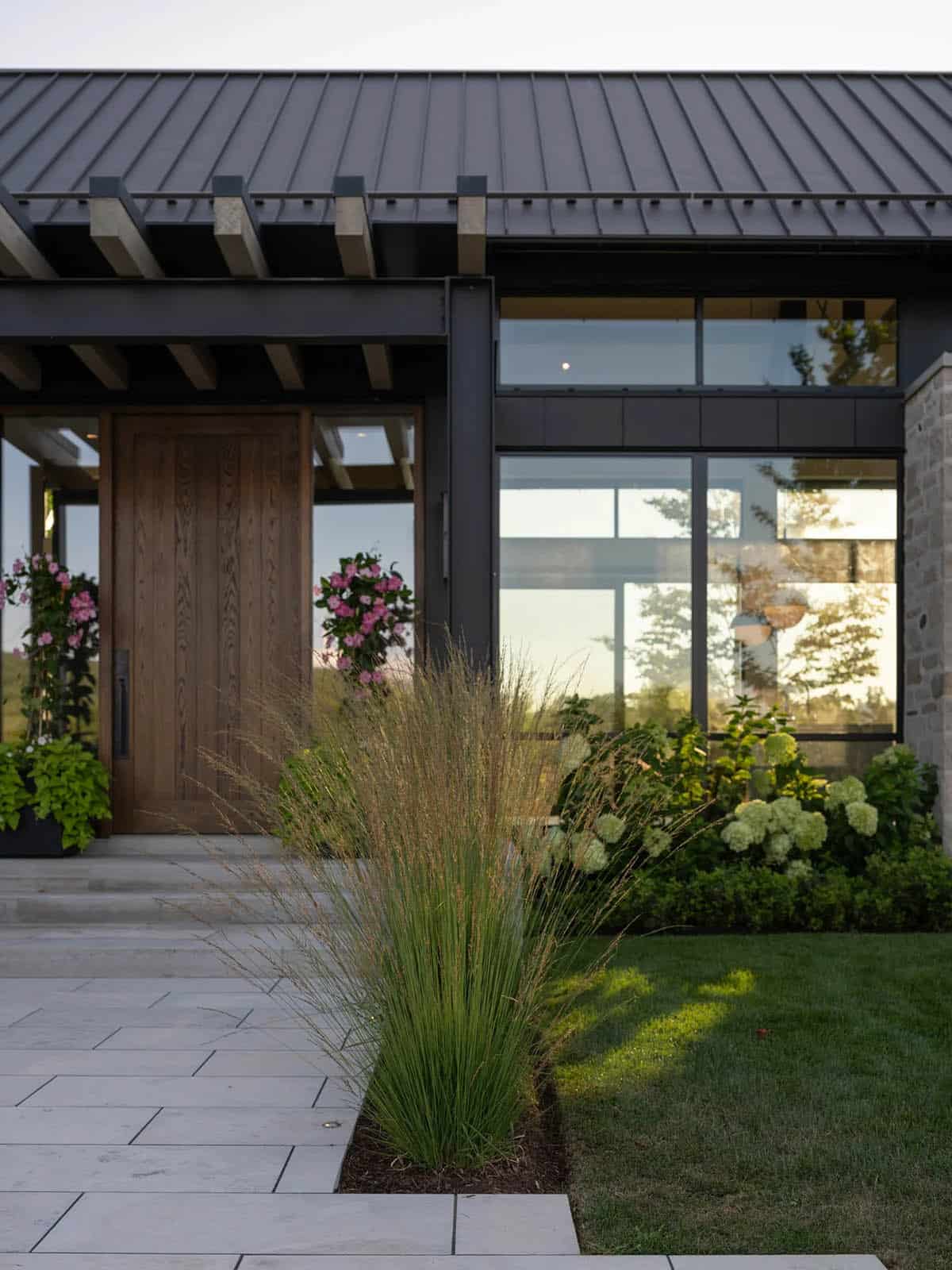 Front entrance with wood door, black steel frame, and native grass landscaping