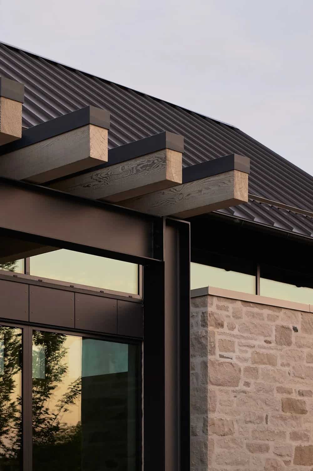Close-up of wood pergola beams meeting black steel column and stone wall