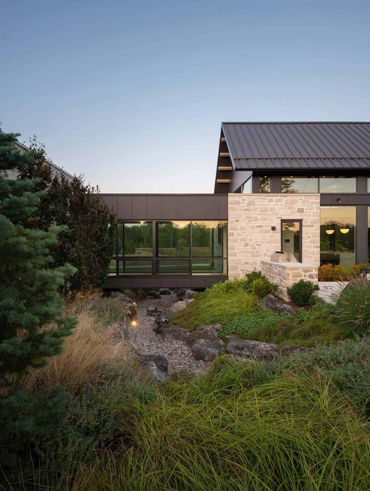 Stone-clad wing of home with outdoor kitchen and dry creek bed landscaping