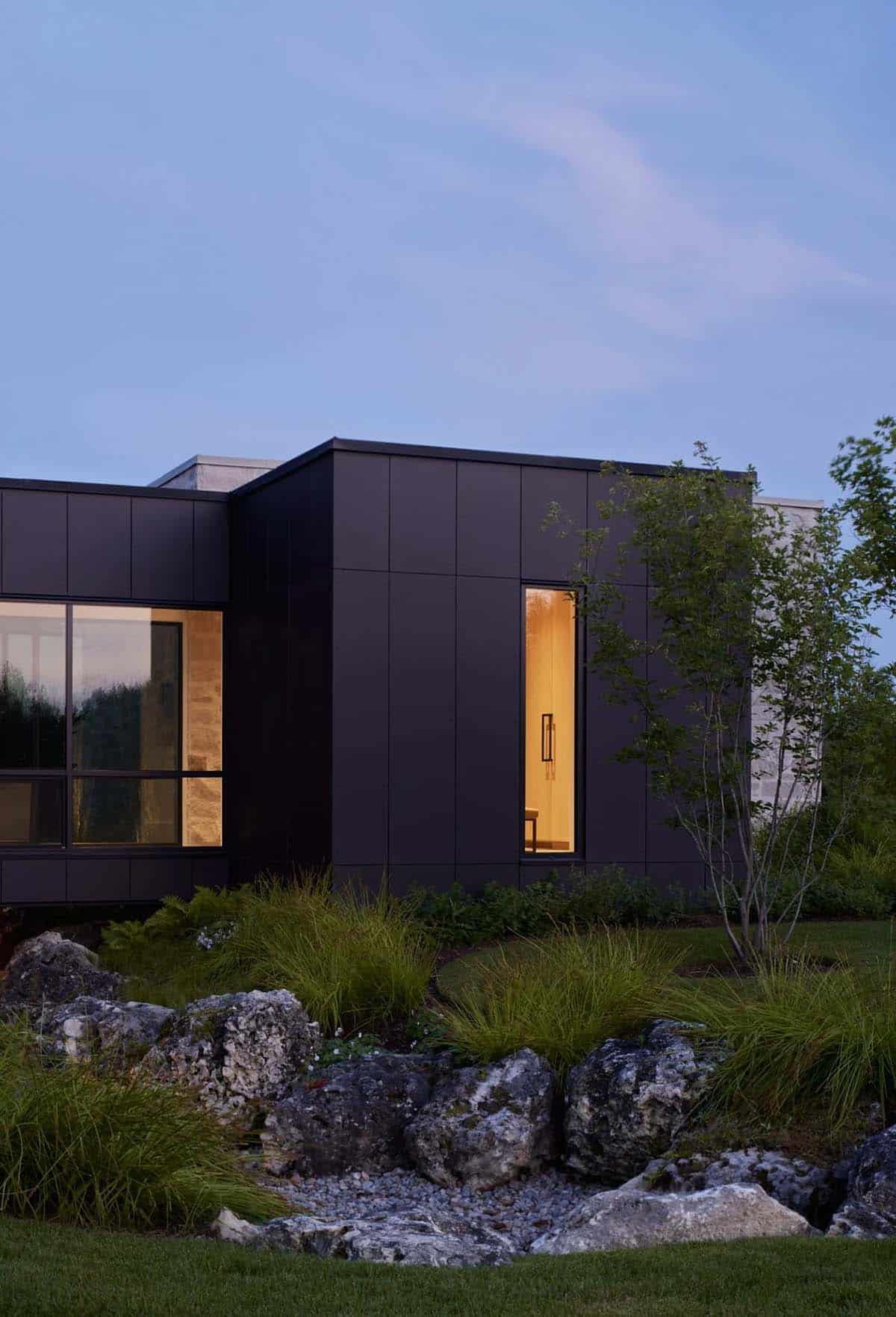 Dark metal-clad addition with glowing interior window at twilight