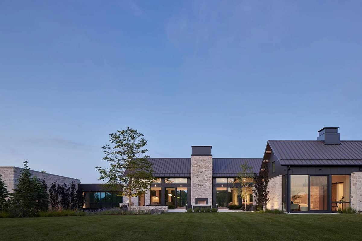 Rear facade at dusk with stone chimney and expansive lawn