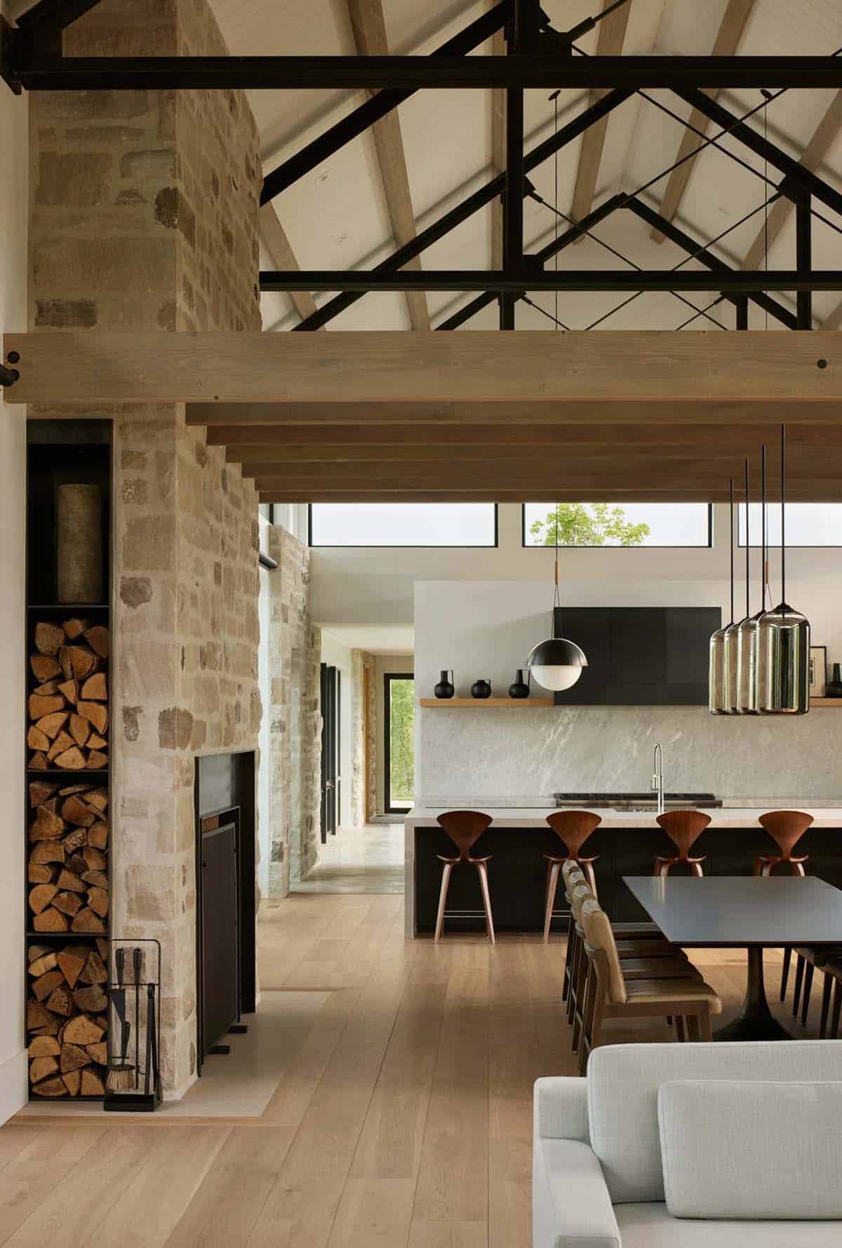 Open living and kitchen area with stone fireplace, firewood storage, and dining table