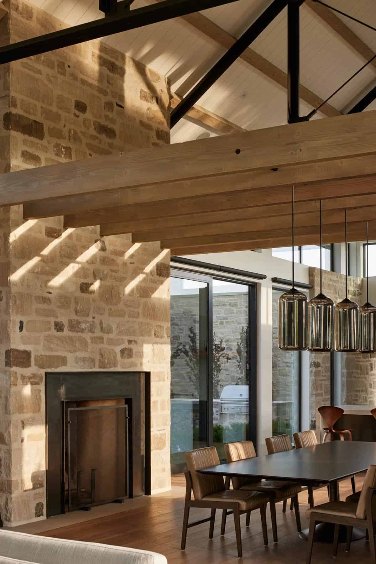 Dining area beneath wood beams with stone fireplace wall and glass doors