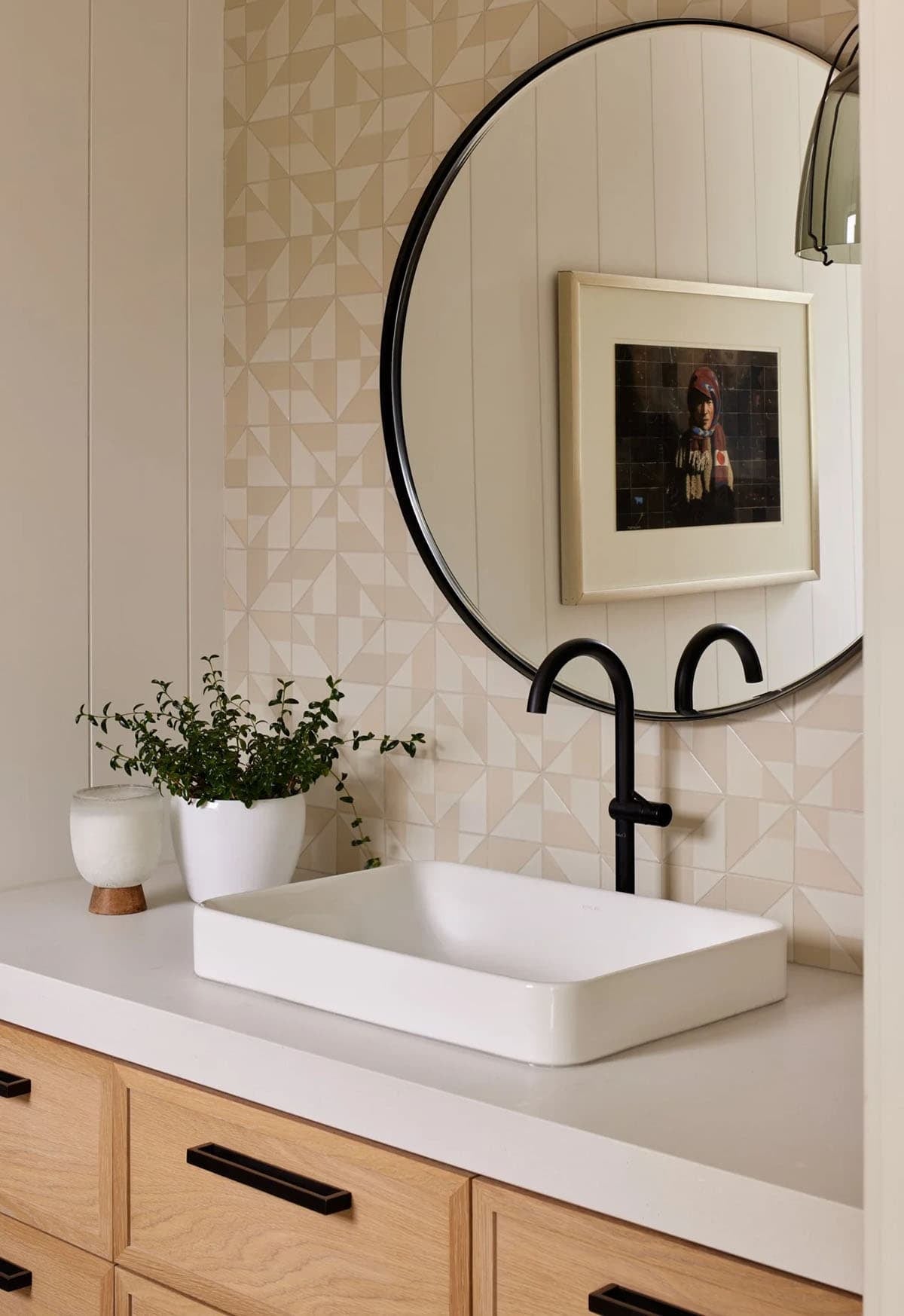 Bathroom vanity with round black-framed mirror and geometric tile backsplash