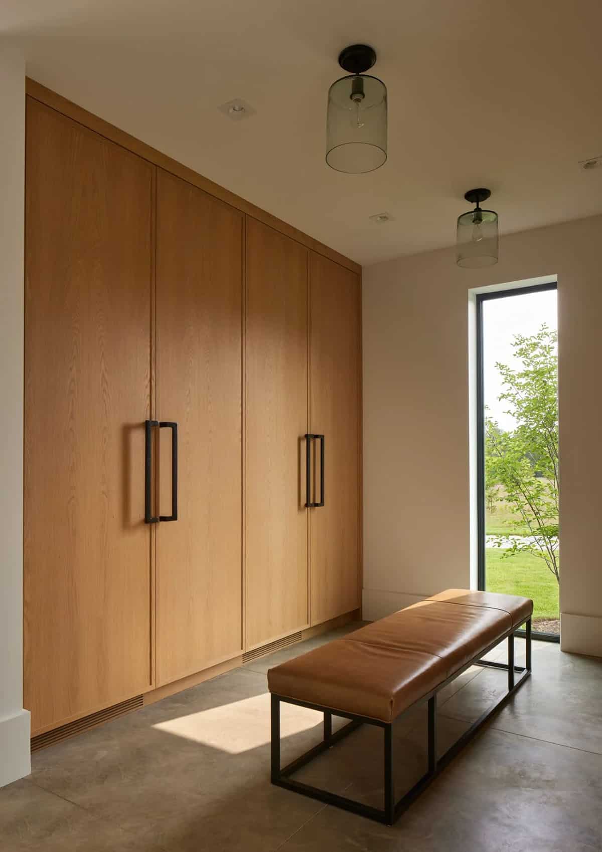 Mudroom with built-in wood cabinets, leather bench, and tall window