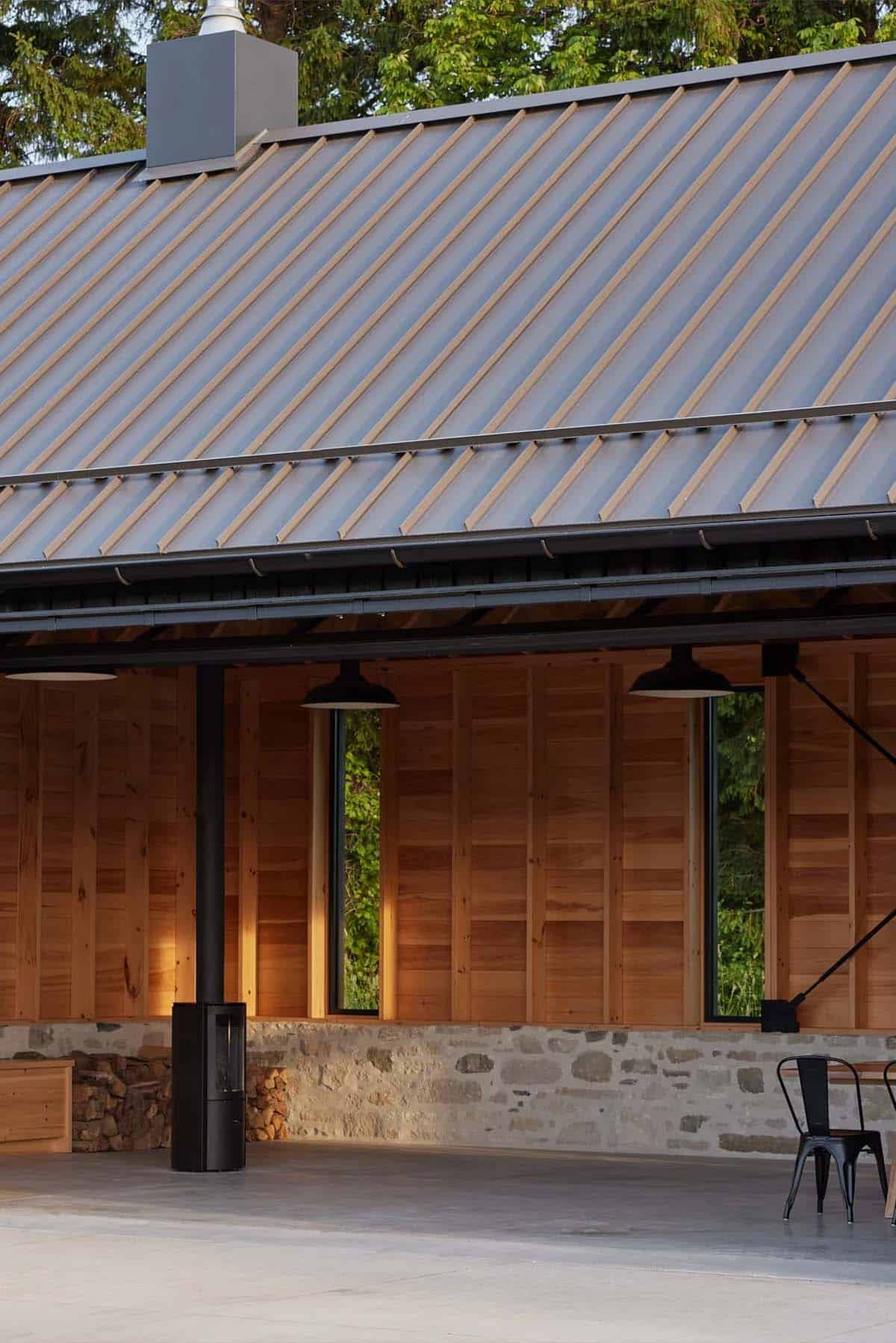Gathering pavilion exterior detail showing wood siding, stone base, and wood-burning stove