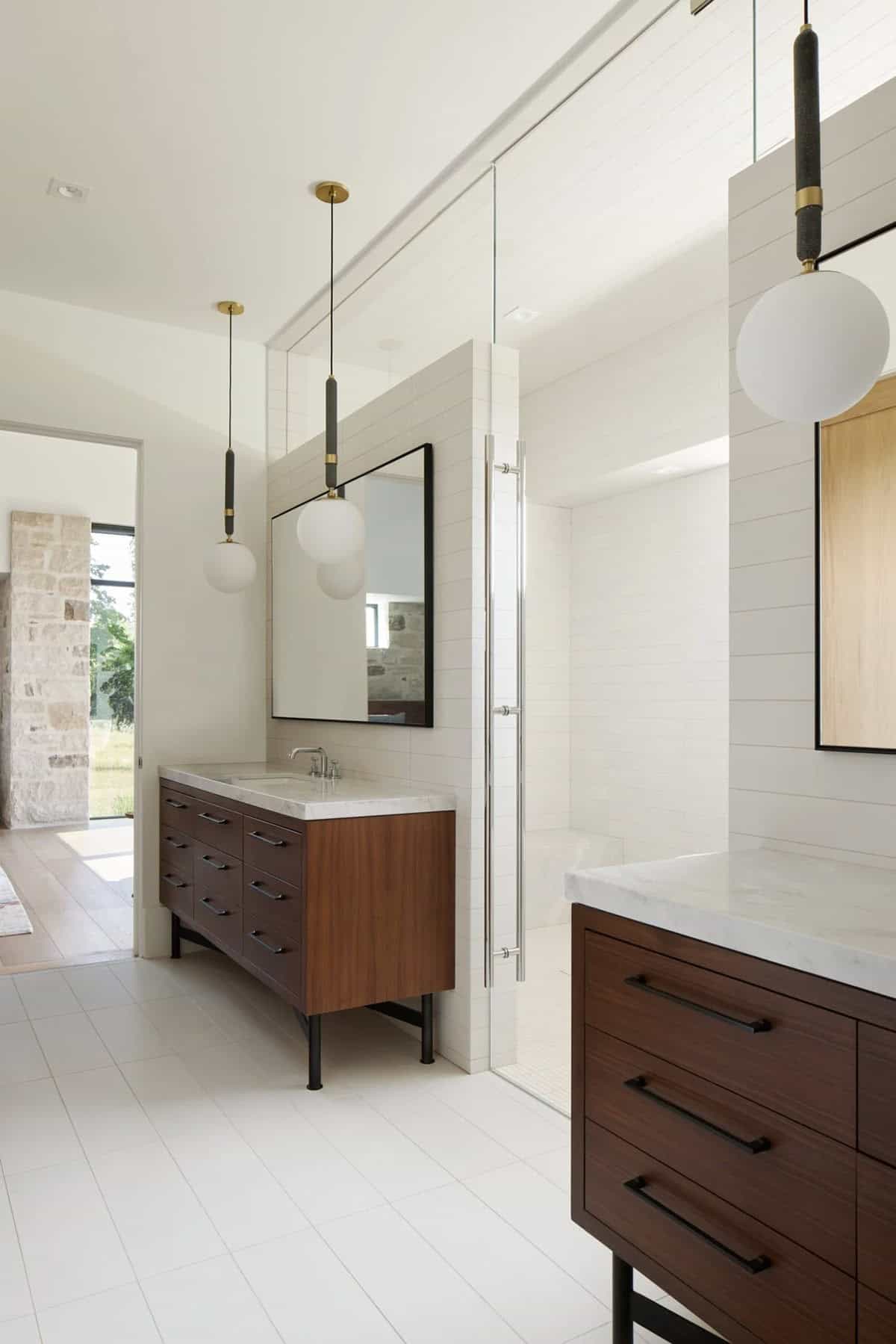 Primary bathroom with walnut vanities, glass shower, and globe pendant lights